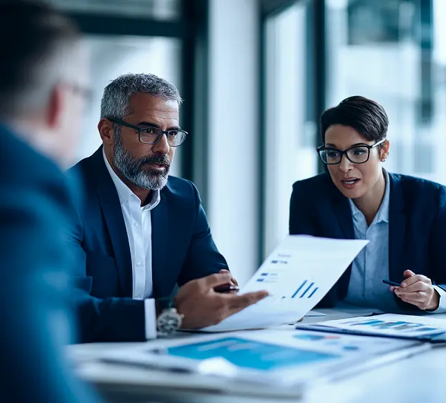 Three business people reviewing charts and reports in a meeting